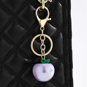 Detailed close-up of a pearlescent purple apple keychain with gold-plated hardware and leaf