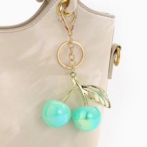 Mint green cherry keychain with gold leaf detail hanging on a beige leather handbag