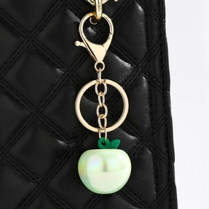 Macro shot of cute light green pear pendant keychain with gold lobster clasp on black bag