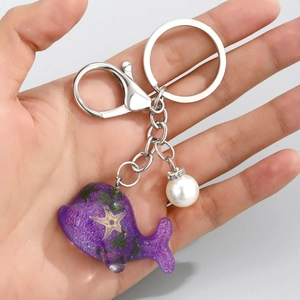 Détail du porte-clés baleine violette en résine avec étoile de mer, herbe et perle blanche