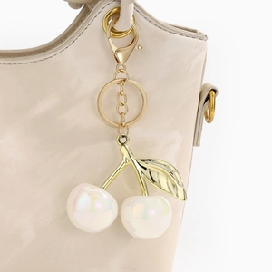 Detail view of pearlescent resin cherry keychain charm with golden leaves on a handbag