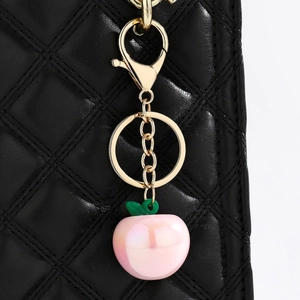 Detailed close-up of pink peach keychain with golden lobster clasp on black leather bag