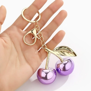 Close-up of purple metallic cherry keychain with golden leaves held in hand