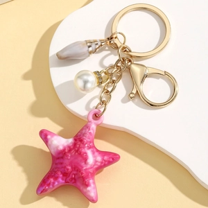 Detail of a gold-tone ocean keychain with pink starfish, pearl, and shell charms