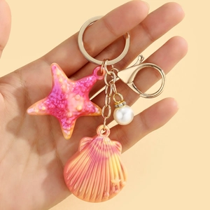 Detail of colorful shell and starfish keychain with pearl and gold clasp in hand