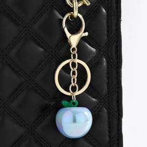 Detailed macro view of pearlescent blue apple keychain on quilted black leather background