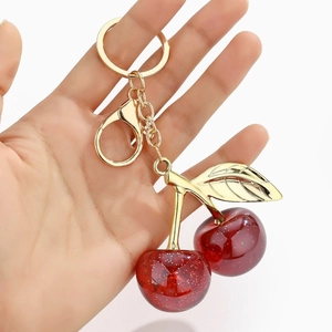 Macro shot of resin cherry keychain with gold leaf held by hand against white background