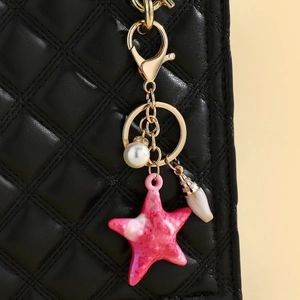 Detail of pink resin starfish keychain with pearl and shell charms on a black quilted bag
