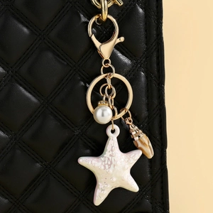 Close-up of starfish, pearl, and shell charms on a gold lobster clasp for bags