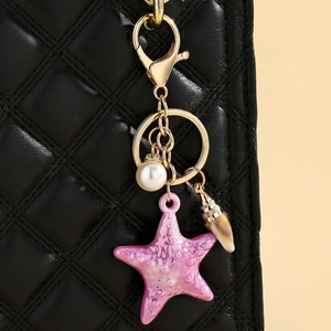 Close-up of pink acrylic starfish charm with pearl and shell on black quilted bag