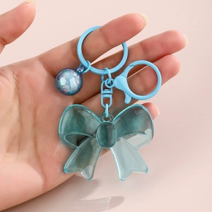 Close-up of cyan acrylic bow keychain with shimmering sphere charm and blue metal hook
