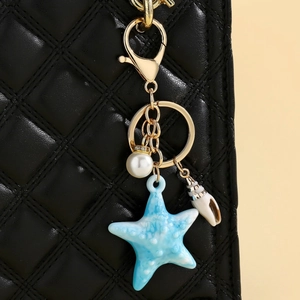 Close-up of ocean-themed starfish keychain with faux pearl on a black quilted bag