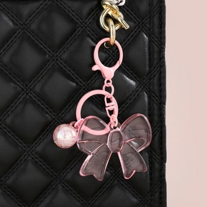Chic pink acrylic bow keychain with shimmering bead on a black quilted handbag