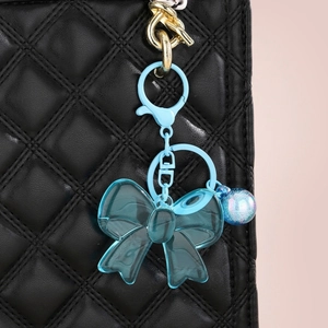 Translucent blue acrylic bow keychain with CD logo heart charm on a black quilted bag