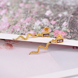 Detail of snake drop earrings with gold finish and rectangular purple zircon stones
