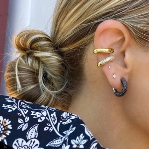 Close-up of stacked C-shaped ear cuffs and studs in gold, silver, and black finish