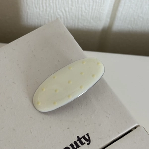 Barrette ovale crème élégante à pois jaunes posée sur une surface à texture douce