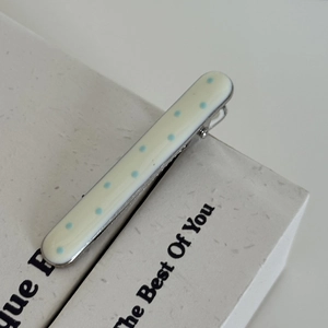 Gros plan d'une pince à cheveux longue en métal avec des pois bleus sur fond beige