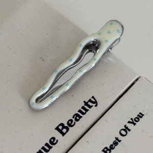Macro d'une pince à cheveux ondulée en métal avec émail crème et pois bleus clairs