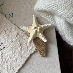 Close-up of starfish hair clip with woven straw base on a rustic linen surface
