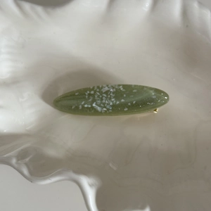 Détail d'une pince à cheveux ovale verte avec paillettes nacrées dans un plat blanc