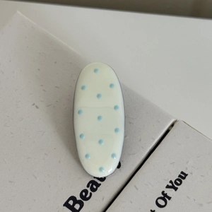 Détail d'une pince à cheveux ovale crème à pois bleu clair sur surface texturée