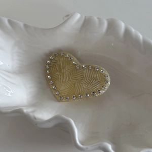 Détail d'une pince à cheveux cœur crème avec texture radiante et strass sur plateau