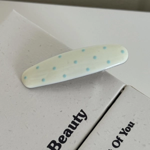 Gros plan d'une pince à cheveux crème à pois bleus sur une boîte cadeau texturée
