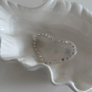 Vue détaillée d'une pince à cheveux en cœur avec strass fins sur un plateau coquillage