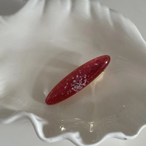 Détail d'une pince à cheveux ovale en résine rouge avec paillettes dorées et blanches