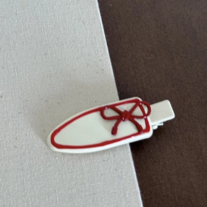 Detail view of a cream hair clip with red bow decoration on fabric texture background
