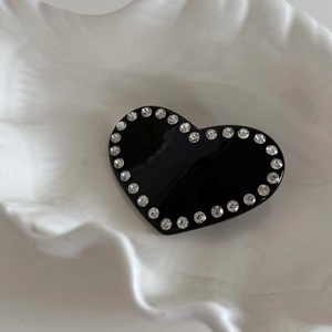 Détail d'une pince à cheveux cœur noir sertie de strass sur un plateau coquille