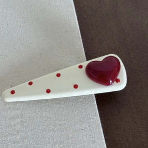 Close-up of a white hair clip with red polka dots and a 3D heart on a fabric background