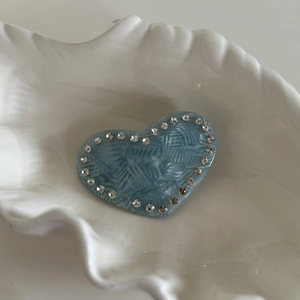 Vue détaillée d'une barrette cœur bleu clair avec strass dans un plat en forme de coquille