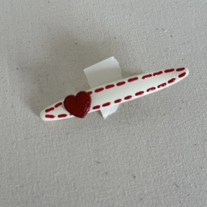 Detail of a white oval hair clip with red dotted edges and a 3D heart on fabric