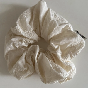 Chouchou blanc avec broderie florale et étiquette de marque sur fond minimaliste