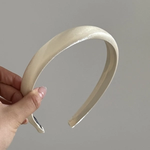 Detail of a padded champagne satin headband featuring a smooth glossy finish and inner lining