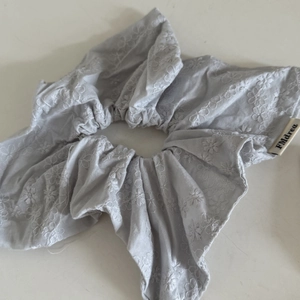 Détail d'un chouchou gris clair avec broderie florale délicate et tissu texturé fin
