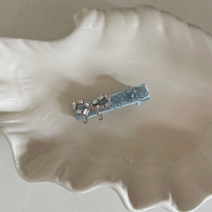 Light blue bow hair clip with sparkling rhinestones on a white shell ceramic tray