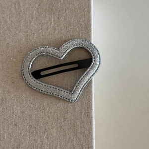 Sparkling silver heart-shaped hair clip with glitter finish on textured beige background