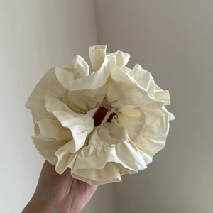 Detailed close-up of large ruffled satin scrunchie in creamy white fabric texture