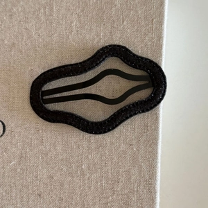 Close-up of black wavy metal hair clip with velvet coating on textured fabric