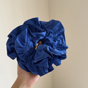 Detailed close-up of large ruffled dark blue satin scrunchie with layered fabric pleats