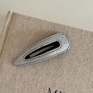 Detail of silver glitter oval hair clip showing fine stitching and secure metal snap base