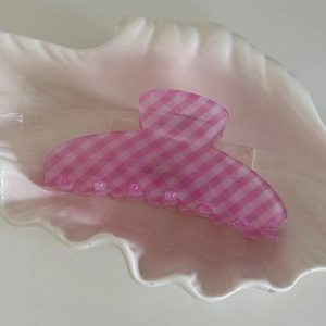 Vue détaillée d'une pince à cheveux à carreaux roses posée sur un plateau coquillage