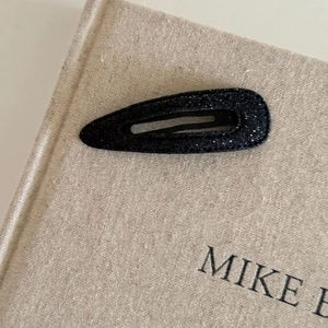 Macro shot of black glitter BB hair clip on textured book surface with subtle shimmer