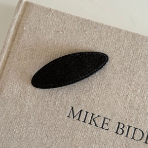 Close-up of black oval BB hair clip with textured fabric surface on a linen book