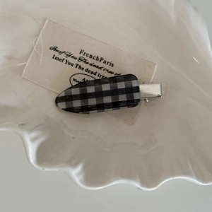 Détail d'une pince à cheveux à damier noir et blanc sur un plateau pour un style minimaliste