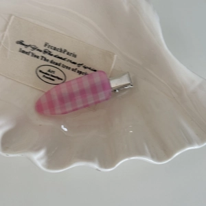 Vue détaillée d'une pince à cheveux à carreaux rose et blanc sur plateau coquillage