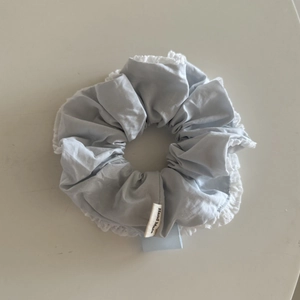 Detail of light blue cotton scrunchie with white lace edges and handmade woven label